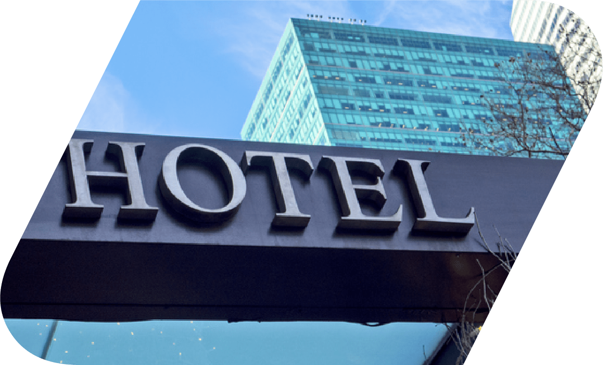 Signage of a hotel on the outside with a skyscraper building in the background.